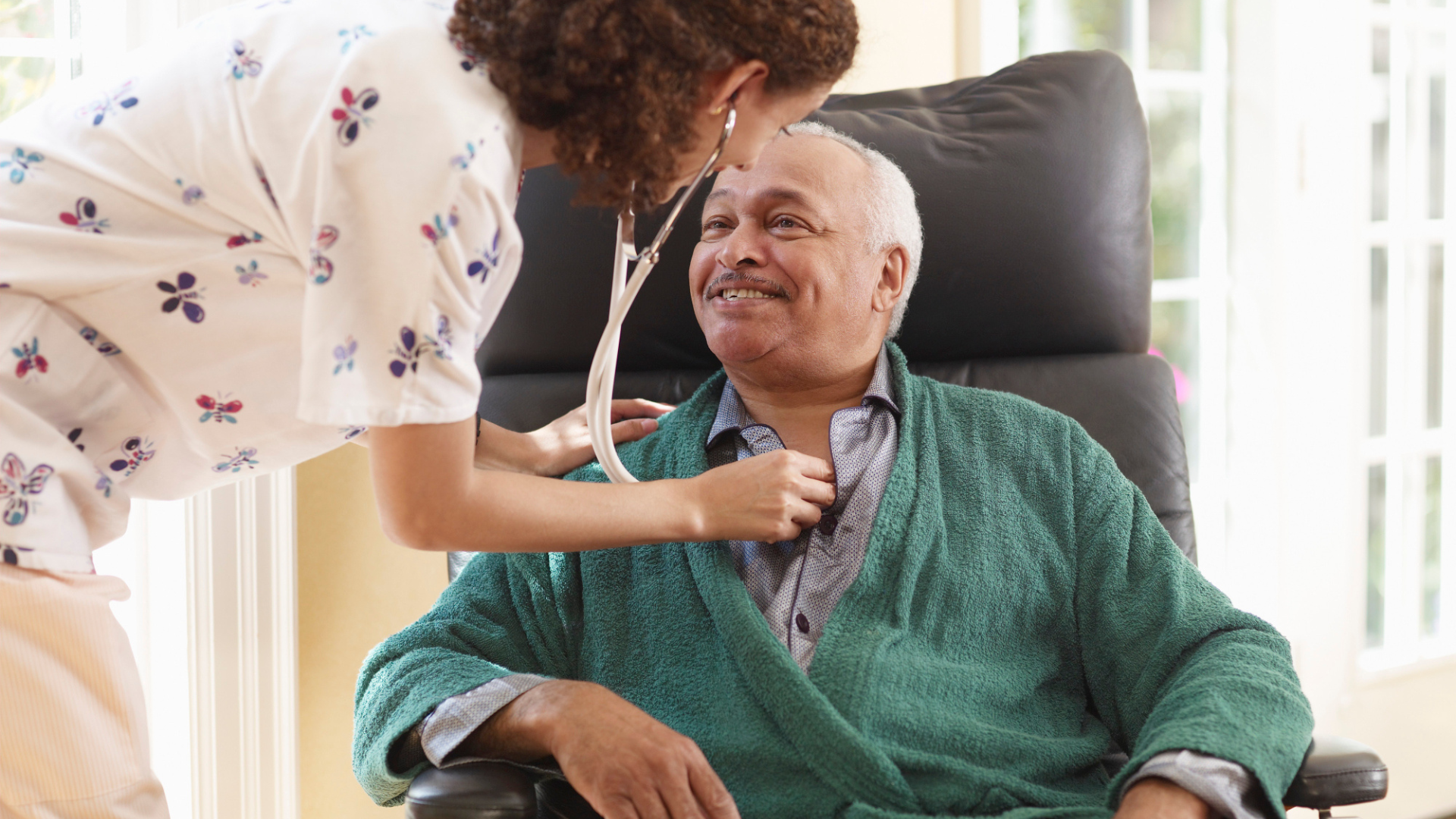 Caregiver checking an elderly man’s heart with a stethoscope in a bright home setting