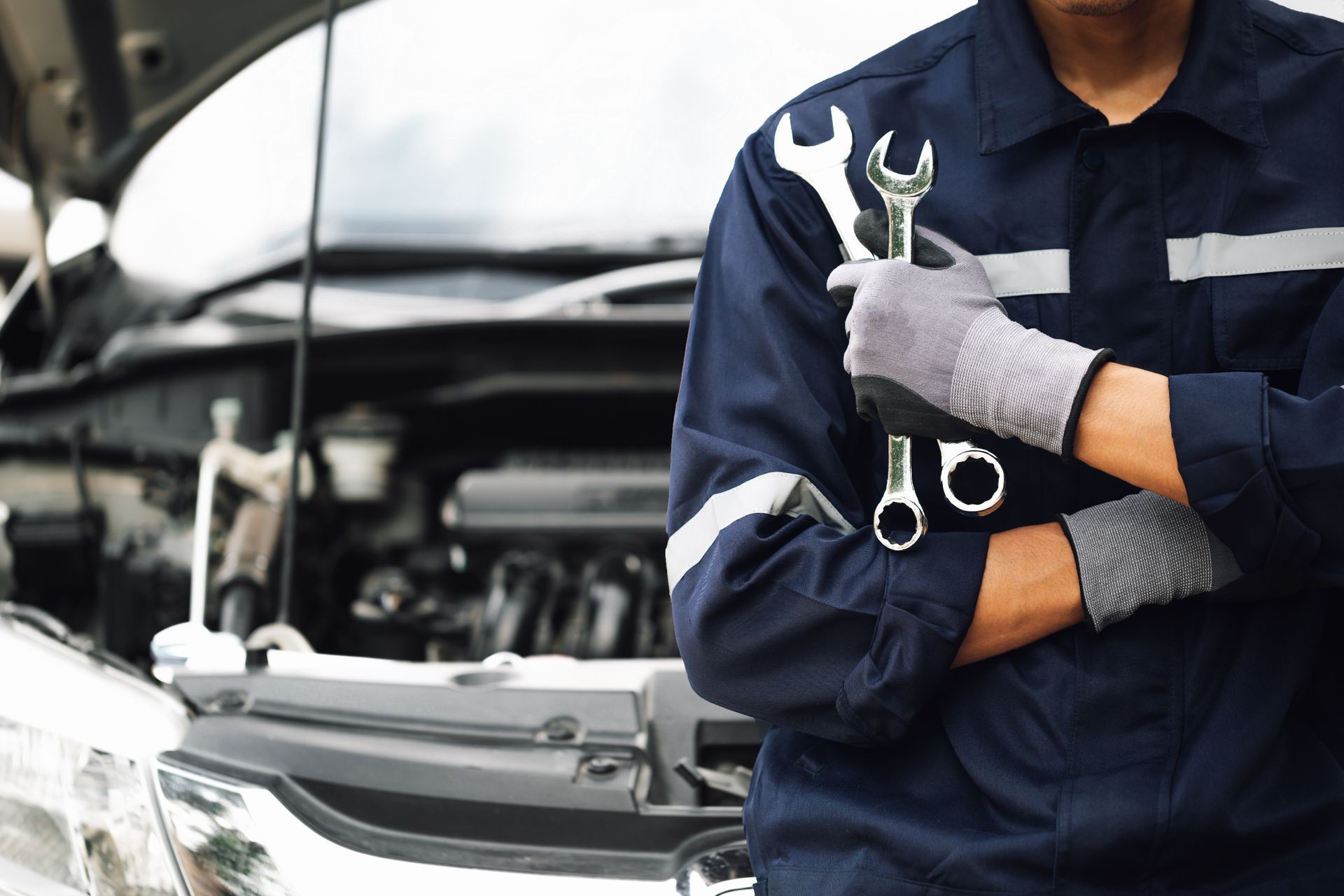 Mechanic in navy uniform holding a wrench beside an open car hood