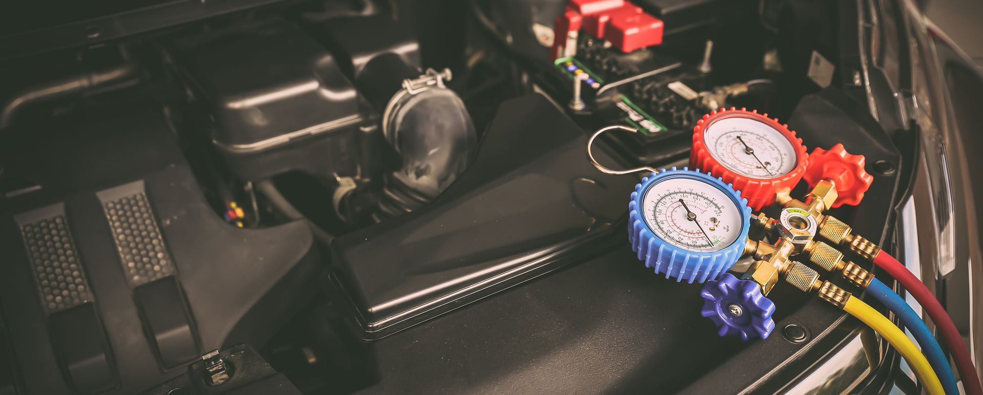 Blue and red pressure gauges connected to colored hoses inside an engine compartment