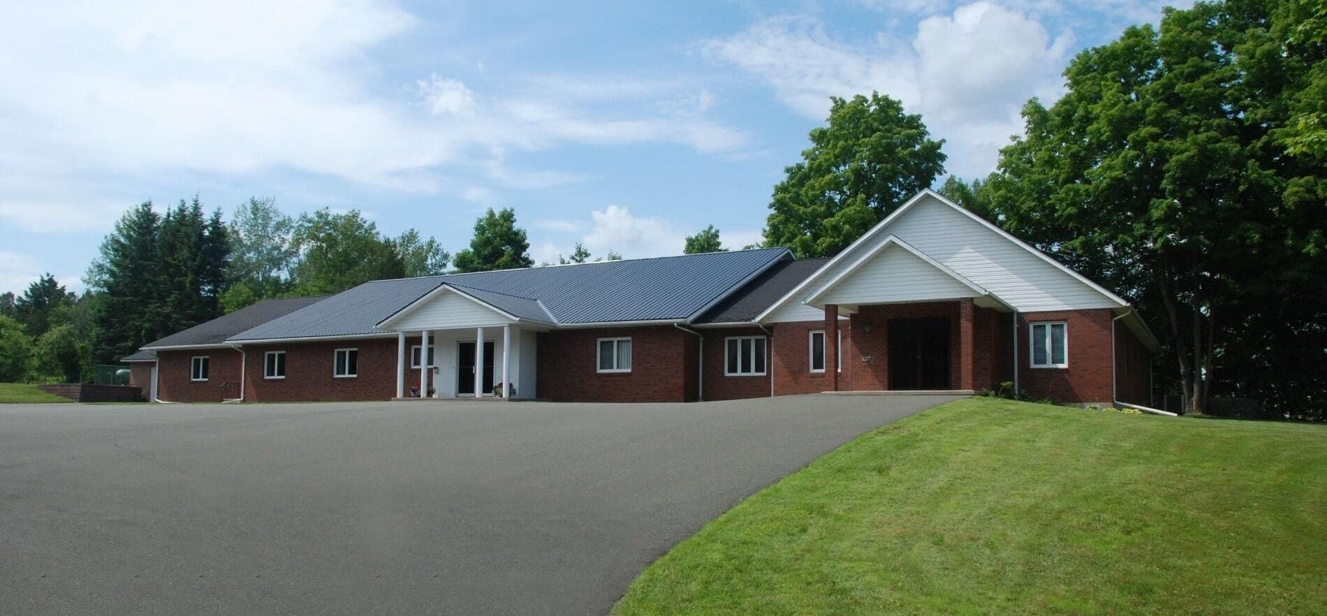 Single-story brick building with a gray roof and wide parking lot under a blue sky