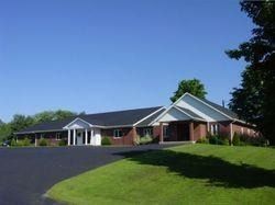 Single-story brick building with white trim on a grassy hill under a clear blue sky