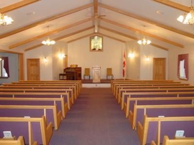 Empty church interior with rows of pews facing the altar, warm lights, and a high wooden ceiling