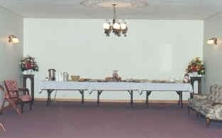 Empty banquet room with a long white-clothed table, floral arrangements, and a chandelier.