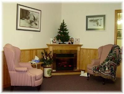 Cozy living room with a fireplace, two striped armchairs, framed art, and a small Christmas tree on the mantel