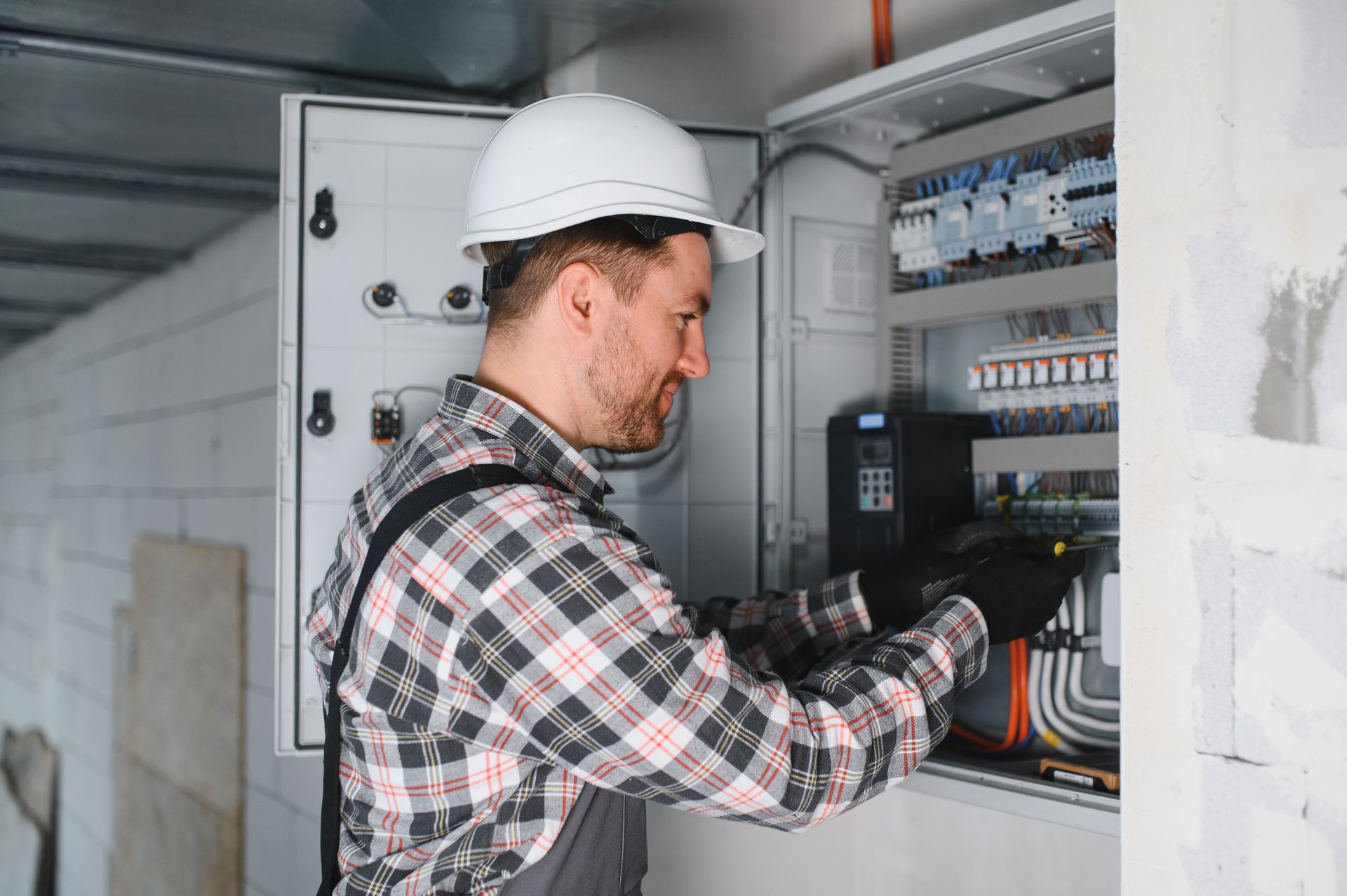 Electrician repairing electrical panel in building under construction.]