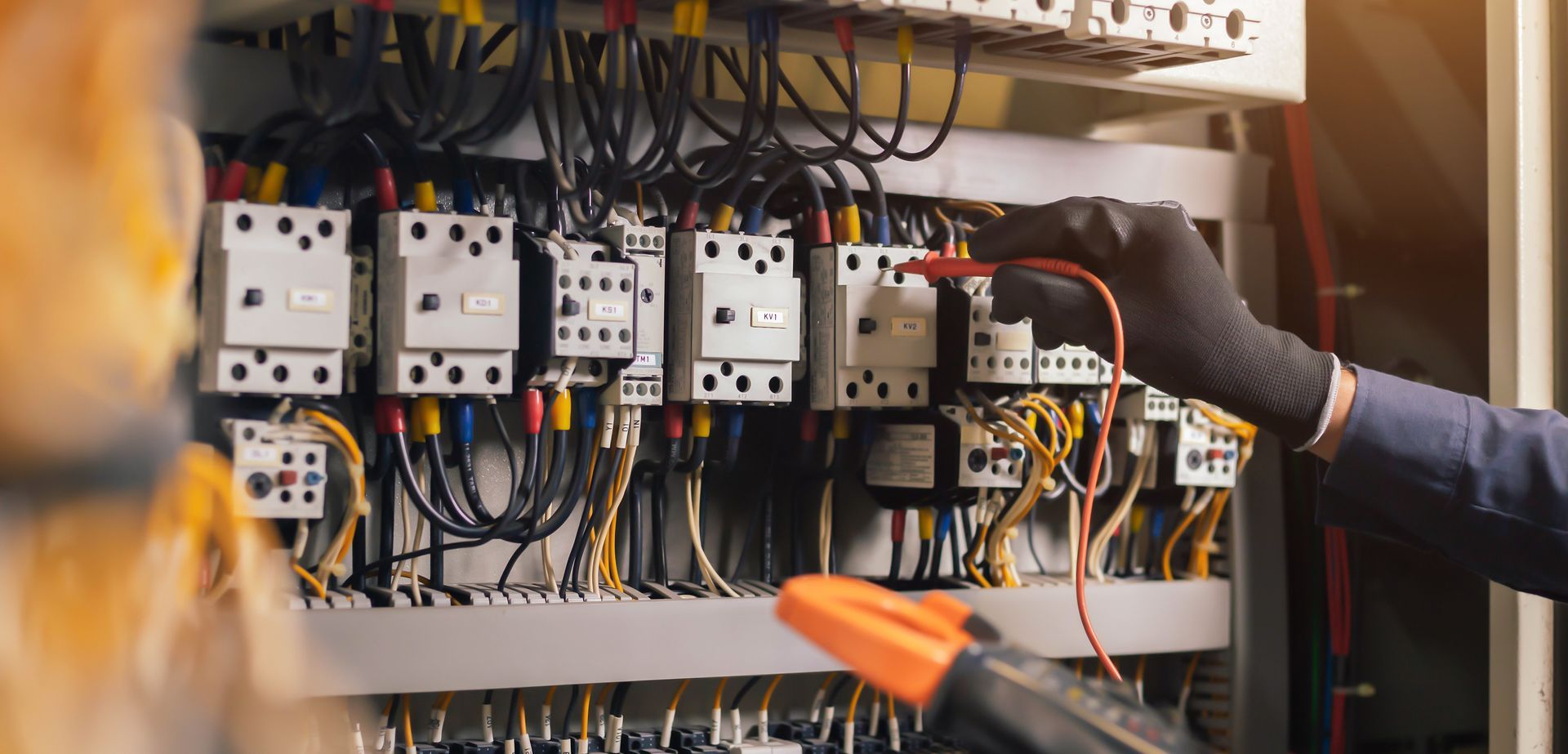 Technician wiring electrical control panel with switches and cables inside an industrial cabinet