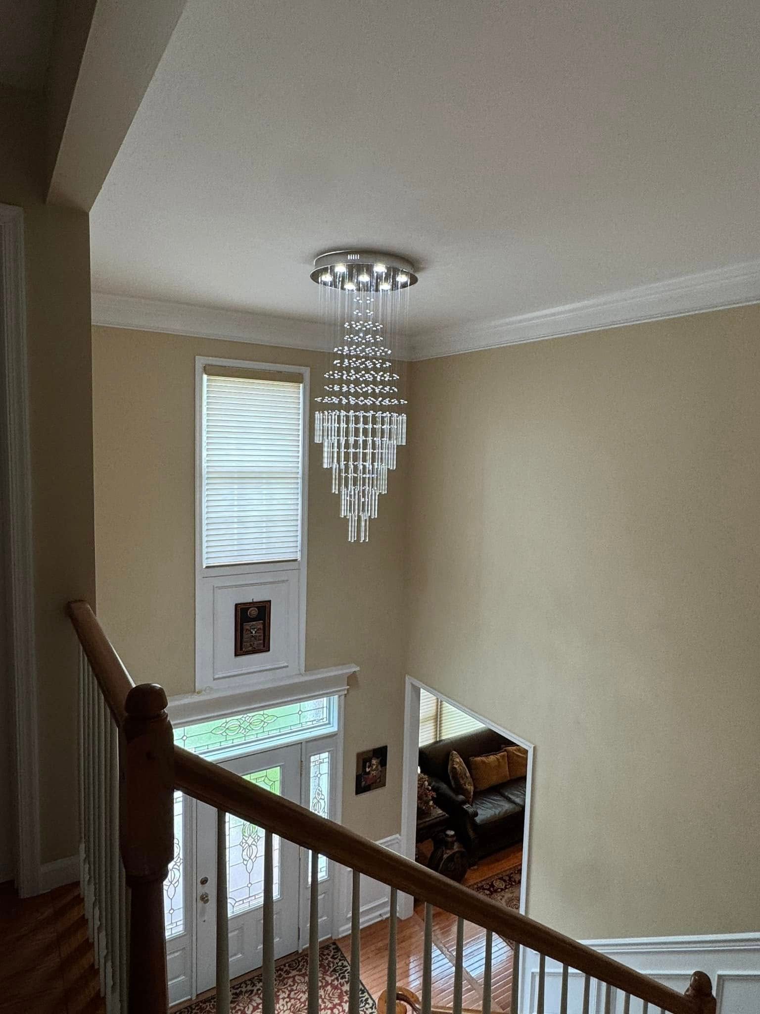 Stairwell with beige walls, wooden railing, chandelier, and front entry visible below.