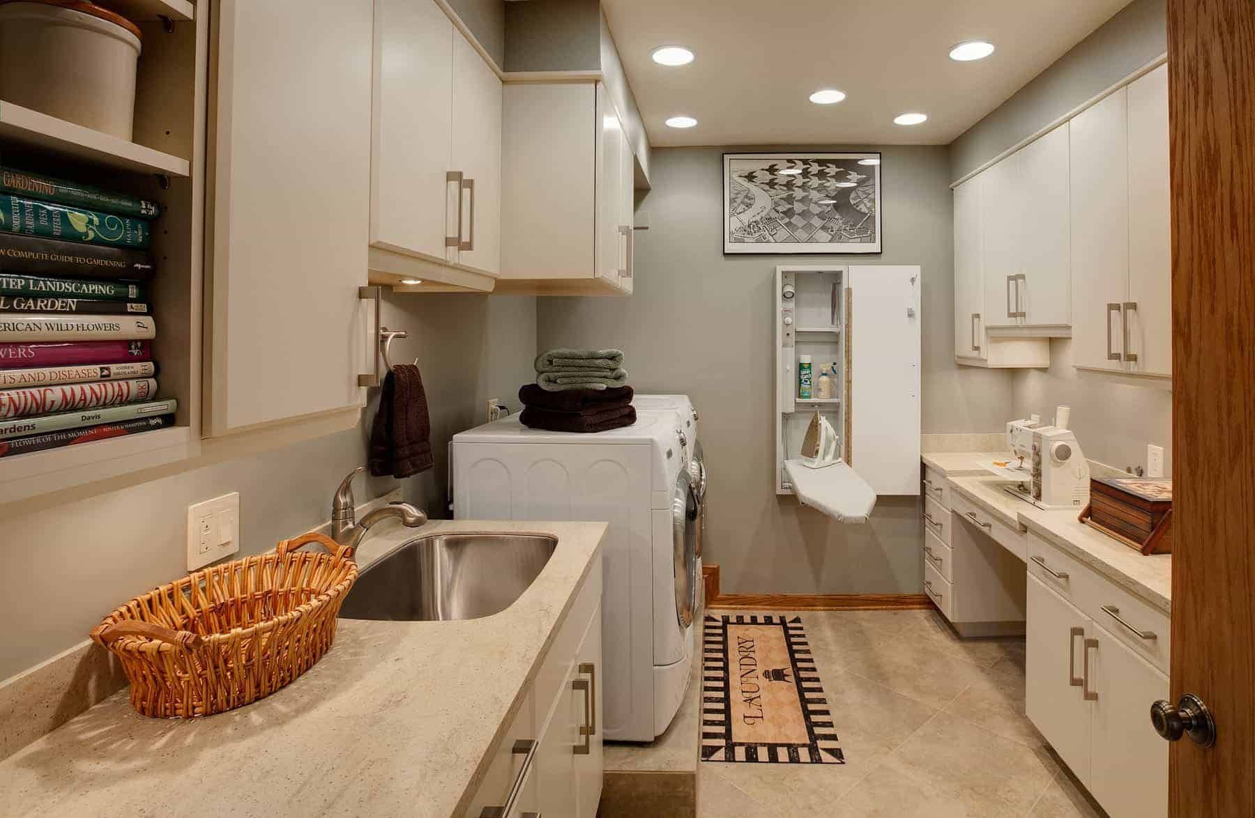 Narrow laundry room with white cabinets, sink, washer and dryer, ironing board, and woven basket.