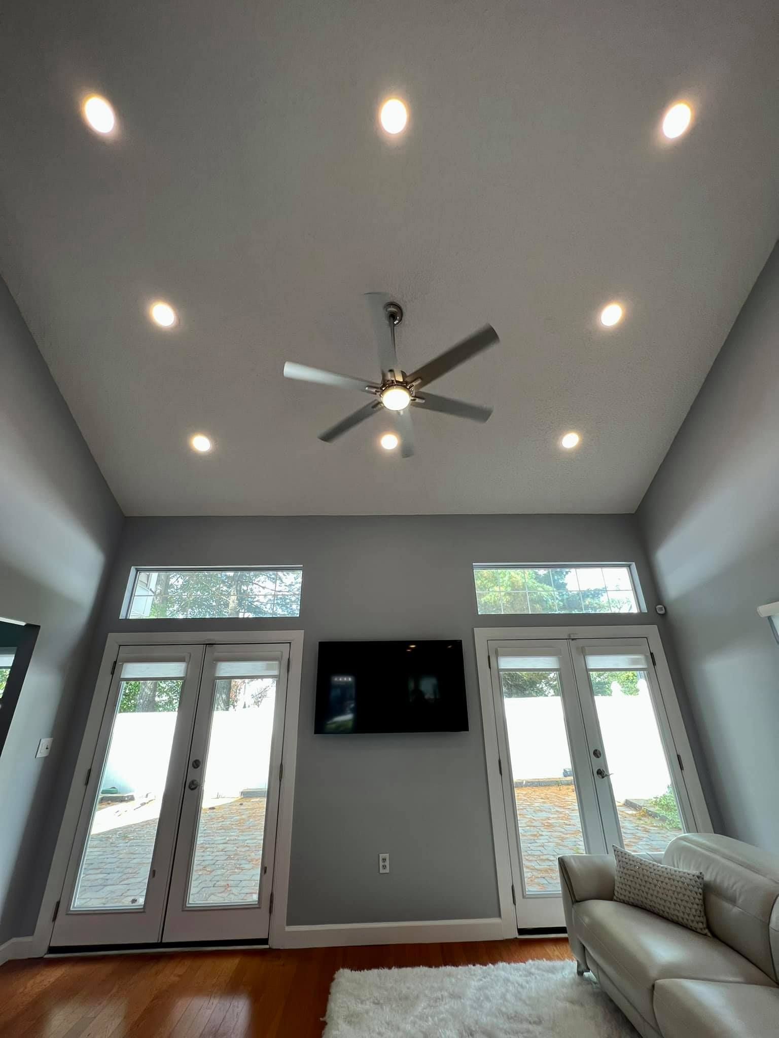 Bright living room with vaulted ceiling, recessed lights, ceiling fan, TV, and white French doors.
