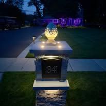 Lit porch memorial with glowing pineapple lantern on a pillar at dusk, house lit purple in background