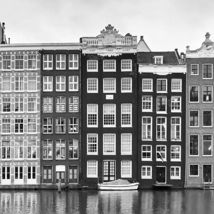 Rij grachtenpanden in Amsterdam, Nederland. Zwart-wit. Een boot ligt aangemeerd voor de gebouwen.