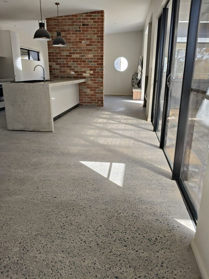 Modern kitchen with Full Exposure concrete floors, a brick accent wall, a central island, and floor-to-ceiling glass doors.