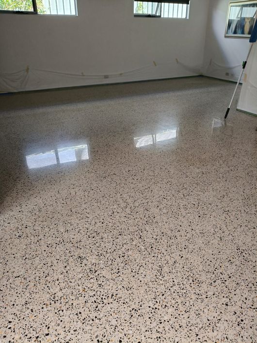 A freshly polished, light-colored terrazzo floor with black and gray flecks, reflecting light in an empty room.