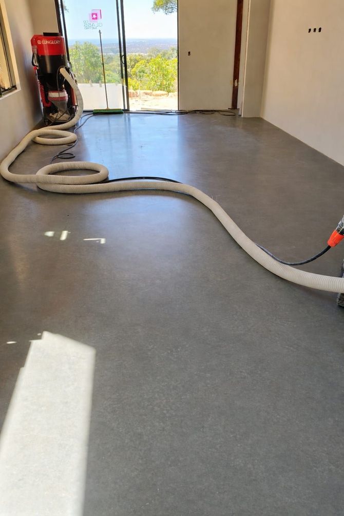 A industrial vacuum cleaner is attached to a long hose across a freshly polished, burnished concrete floor.