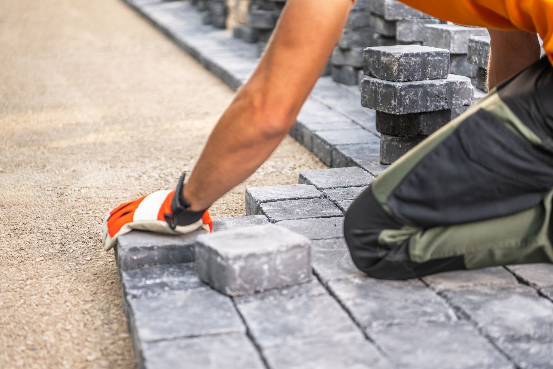A professional paving contractor positions paving stones on a pathway, focusing on alignment.