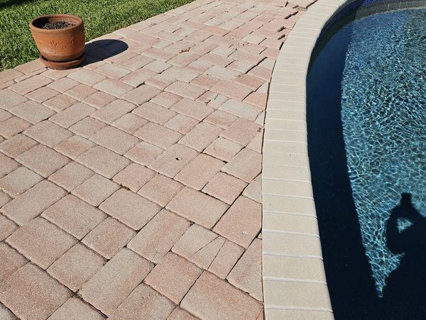 Brick patio next to a swimming pool with a terracotta pot on the grass.