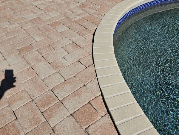Brick patio next to a curved pool with blue water.