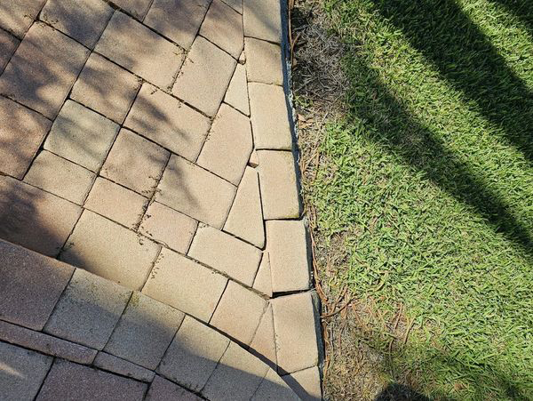 Beige brick patio with broken edge, next to green grass.