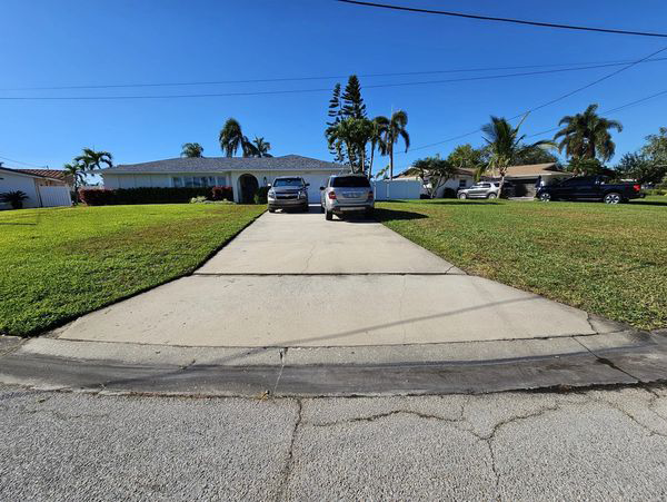 Long driveway leading to a house with two parked cars, bordered by green grass and blue sky.