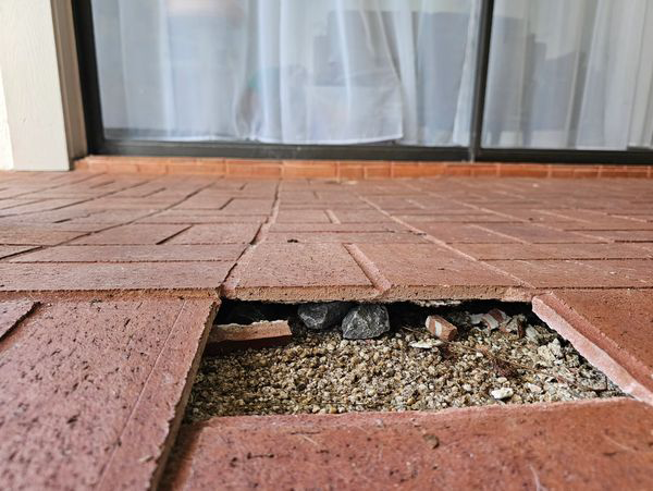 Red brick patio with a missing brick, revealing gravel and stones.