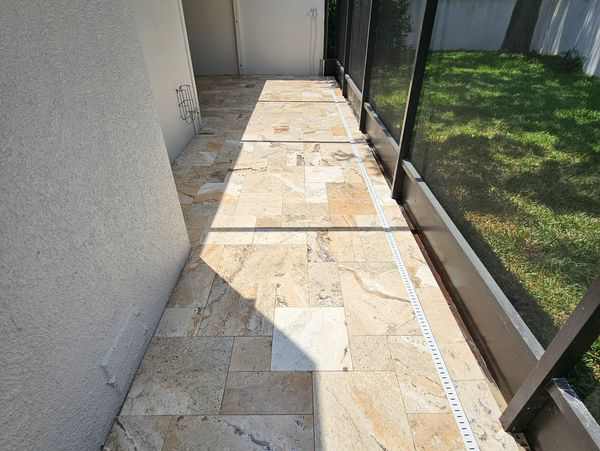 Stone tiled patio with black screened enclosure and green grass. Sunlight casts shadows on the floor.