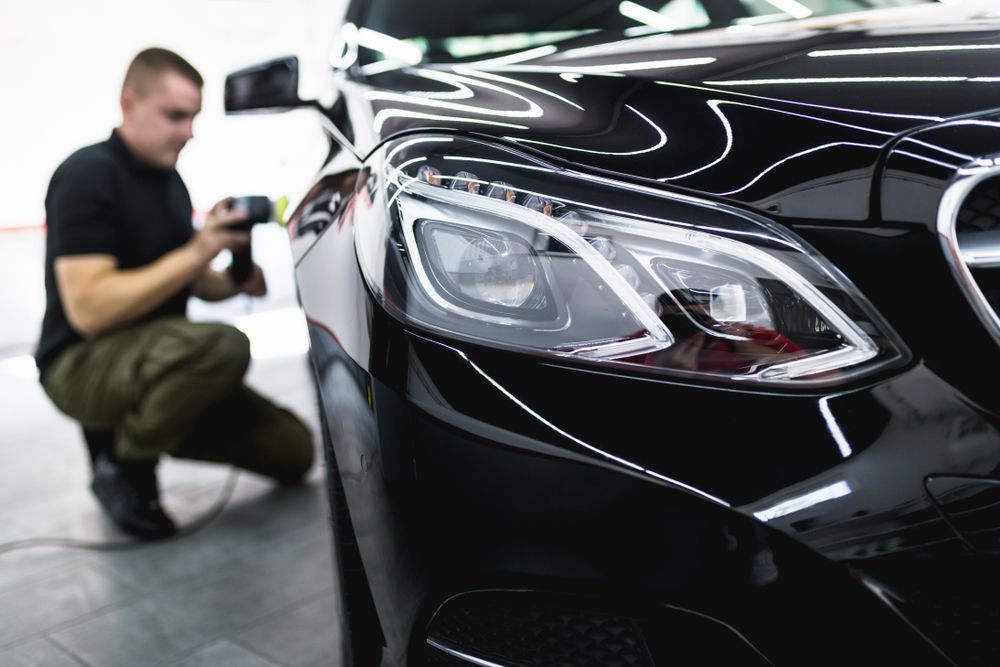 A Man Is Polishing the Headlights of A Black Car — Jetty Car Detailing Coffs Harbour in Coffs Harbour NSW