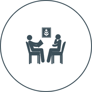 Two people seated in a discussion, with a framed leaf symbol on the wall above them.