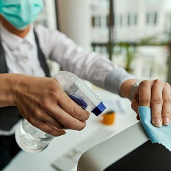 Person spraying disinfectant and wiping a surface with a blue cloth in a clean indoor space