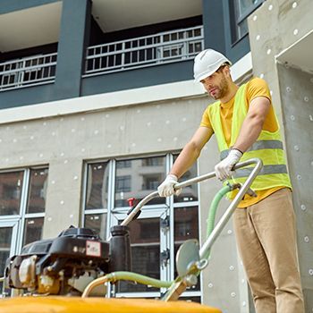 Worker in yellow vest operating a floor machine outside a building under construction