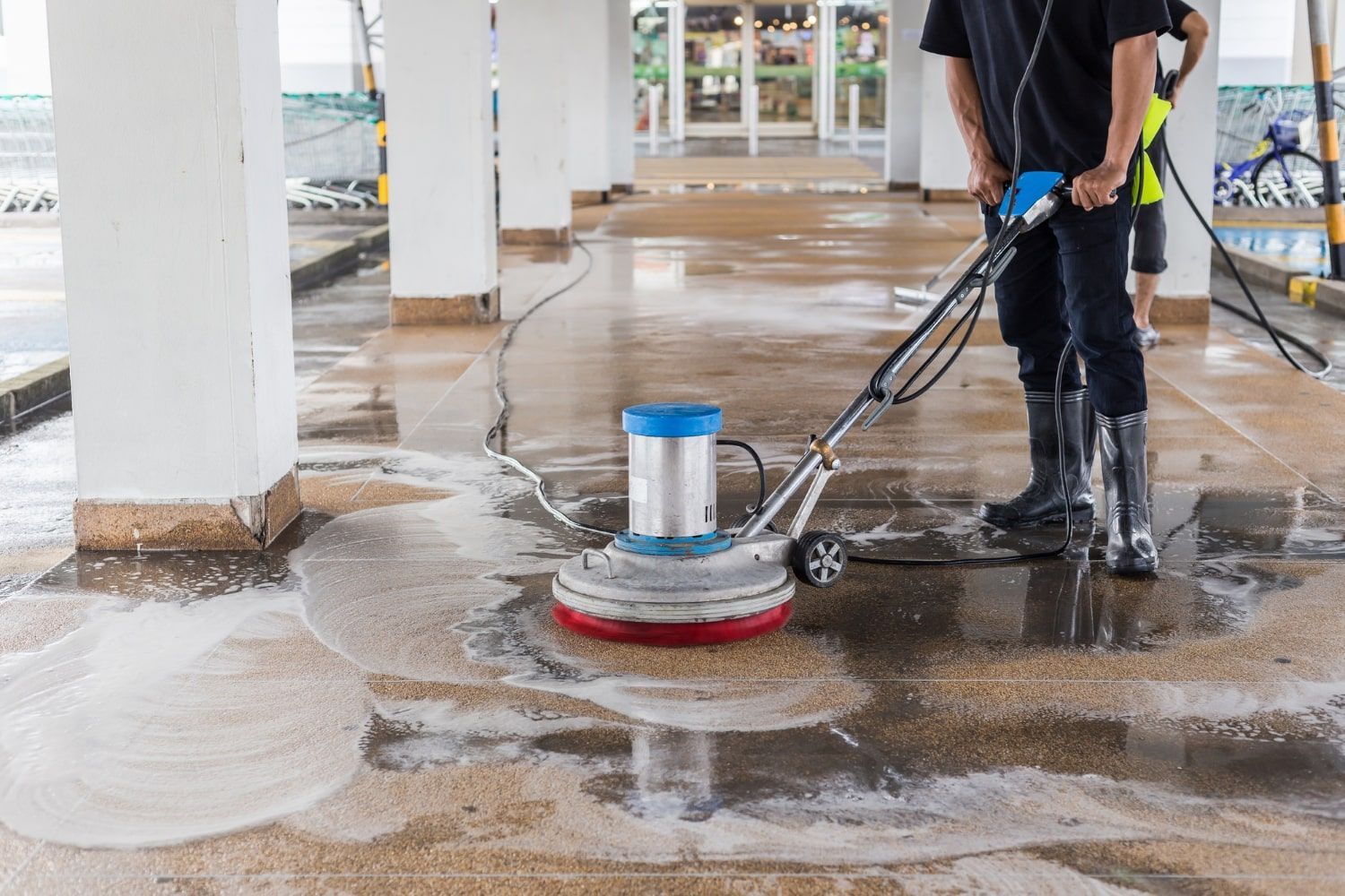 Worker using a floor scrubber to clean a wet concrete floor indoors
