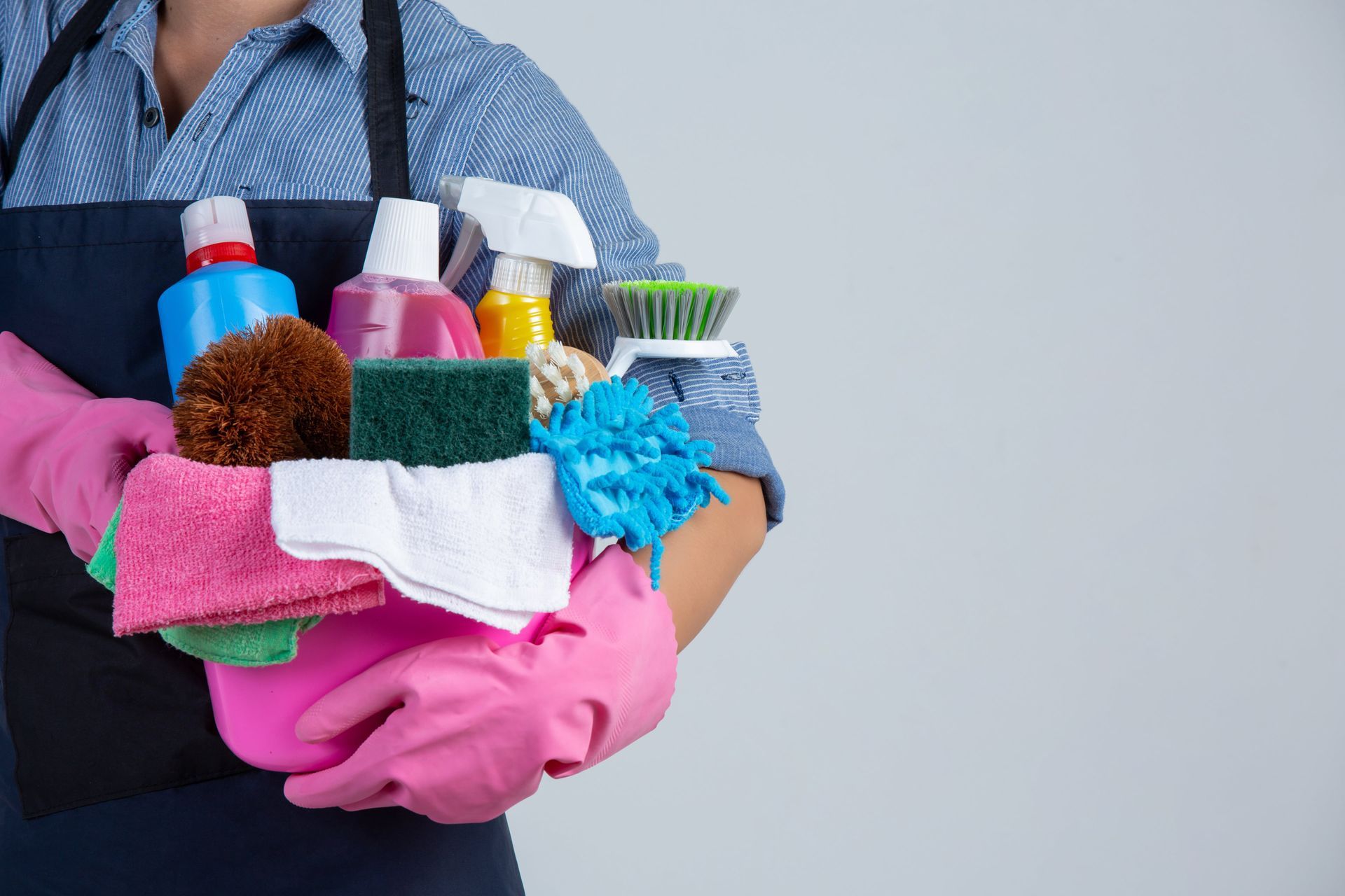 Person holding cleaning supplies and colorful cloths with pink gloves, suggesting house cleaning.