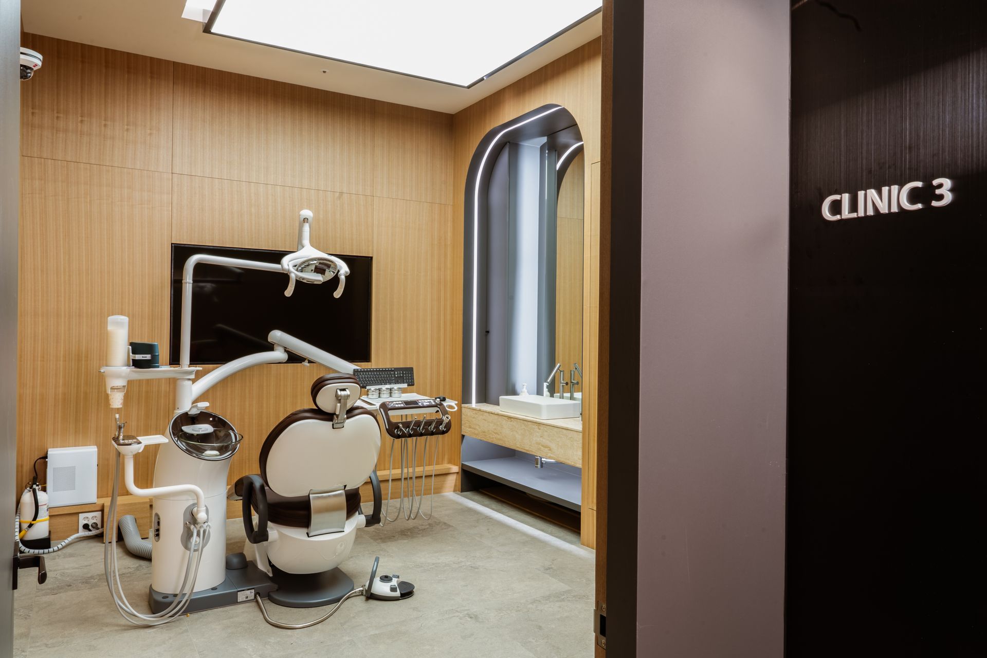 Dental clinic room with dental chair and equipment, wood paneling, and a sink area. 