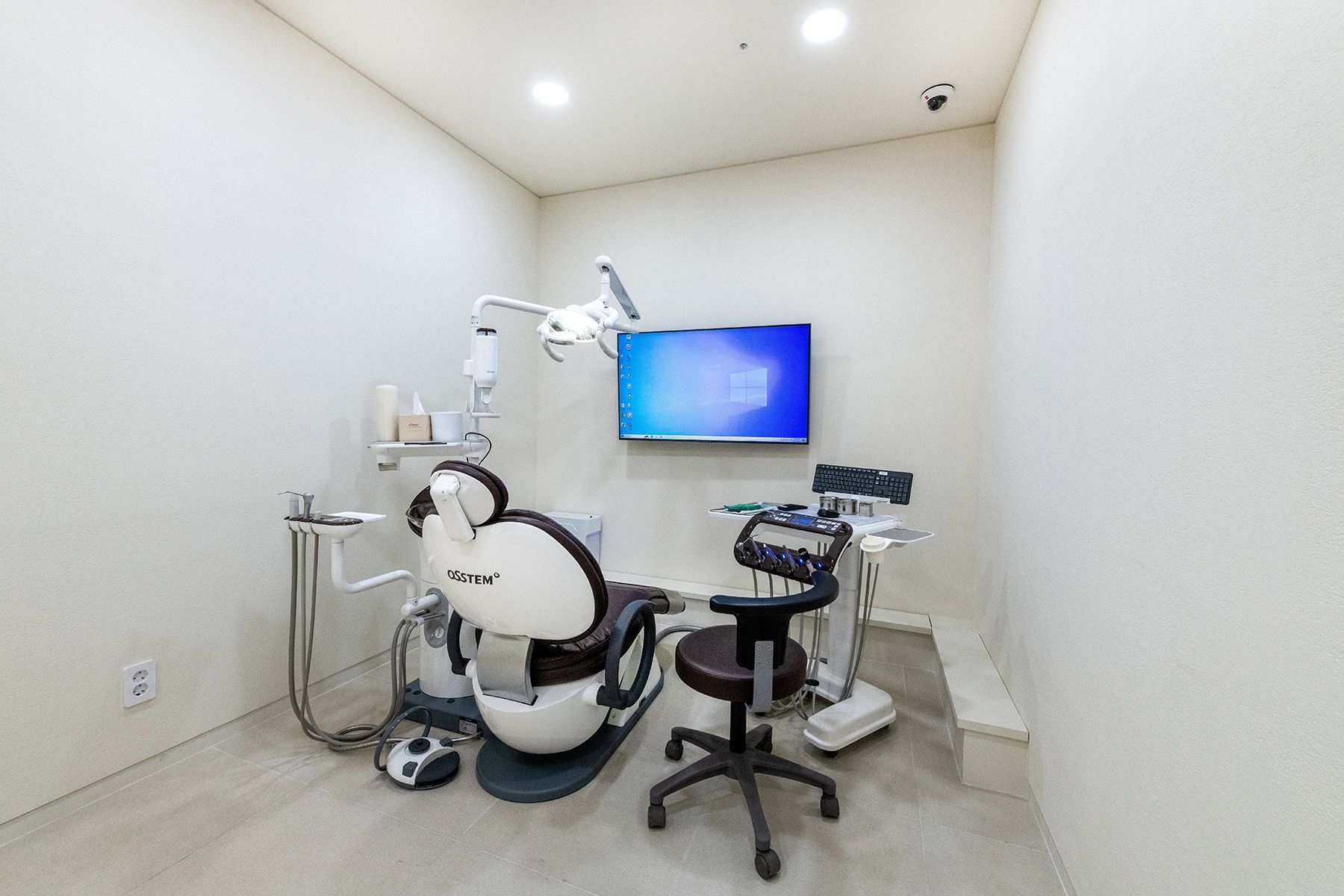 Dental exam room with chair, equipment, and a screen.