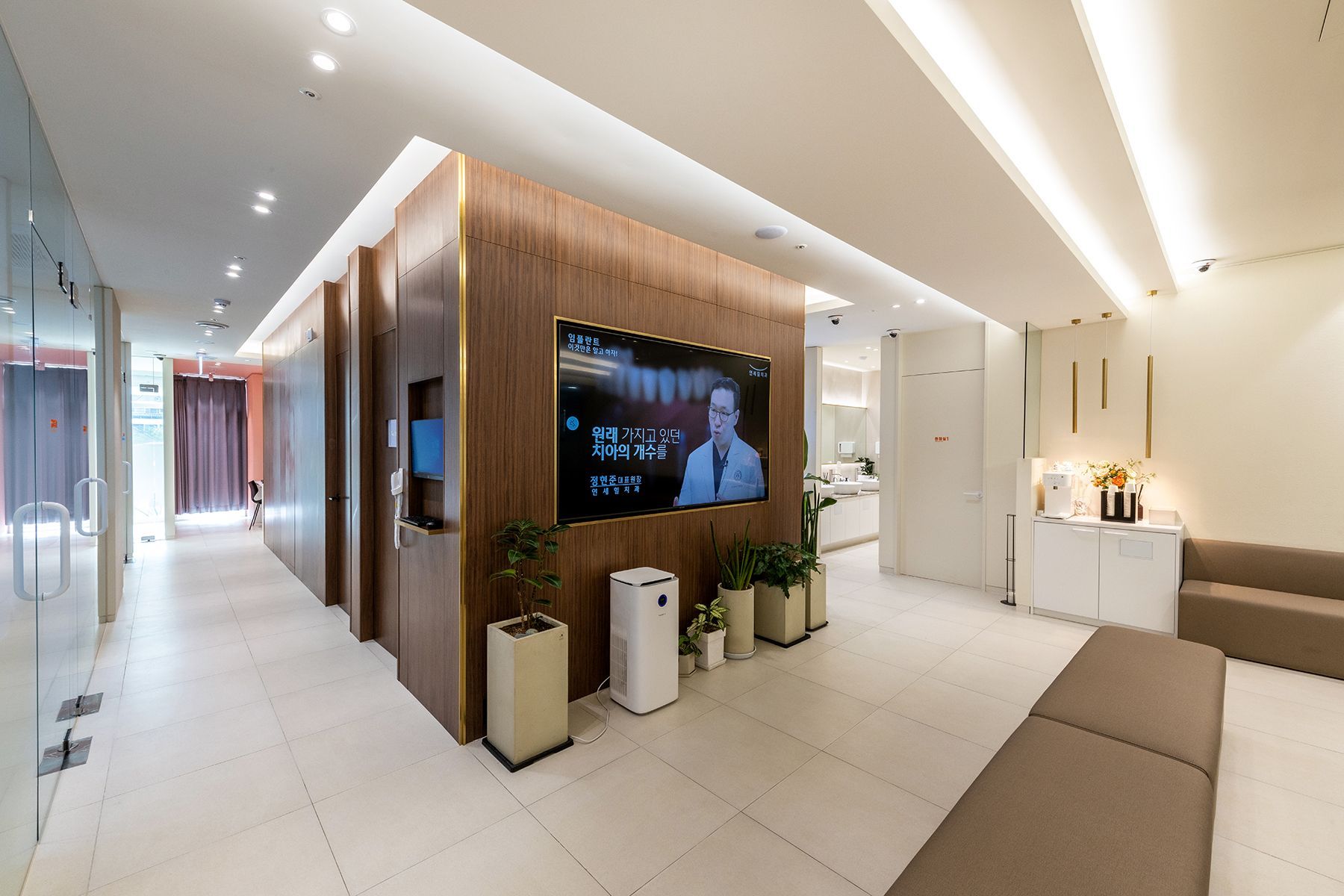 Modern waiting room with wood paneling, large TV, plants, and a long sofa.
