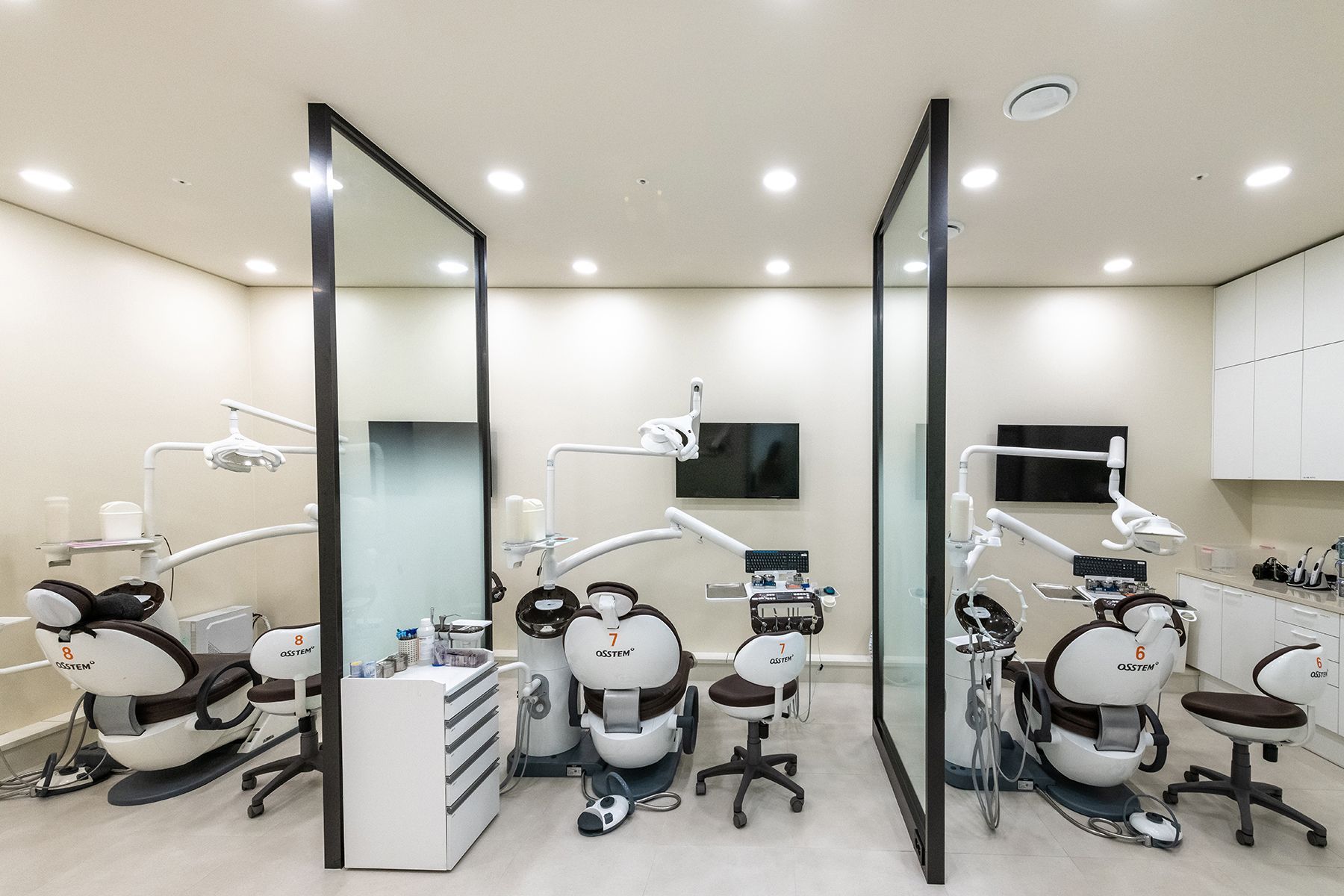 Dental clinic interior with three patient chairs, glass partitions, and medical equipment.