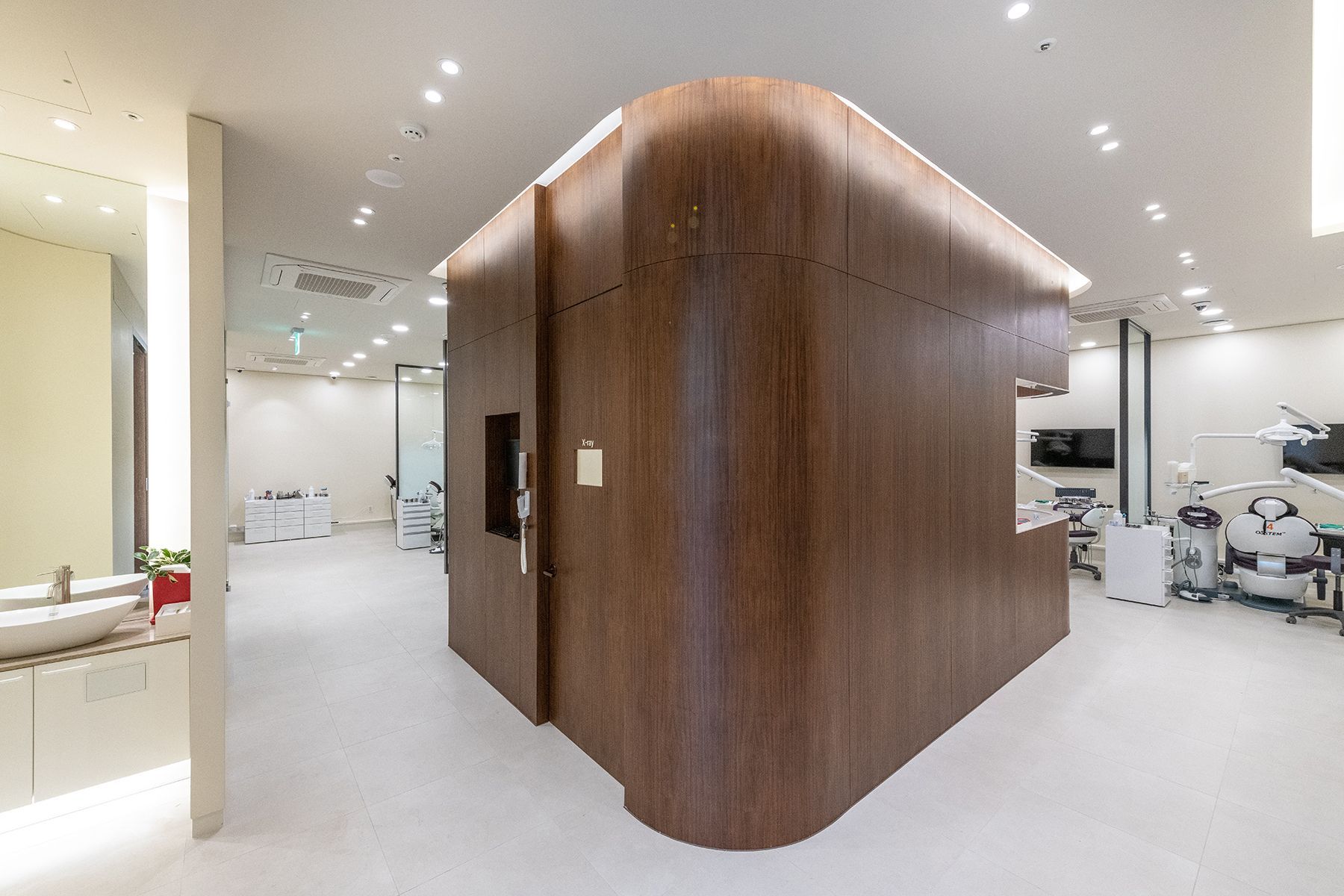 Modern dental office interior with a wooden-paneled reception area, bright white walls, and dental equipment visible.