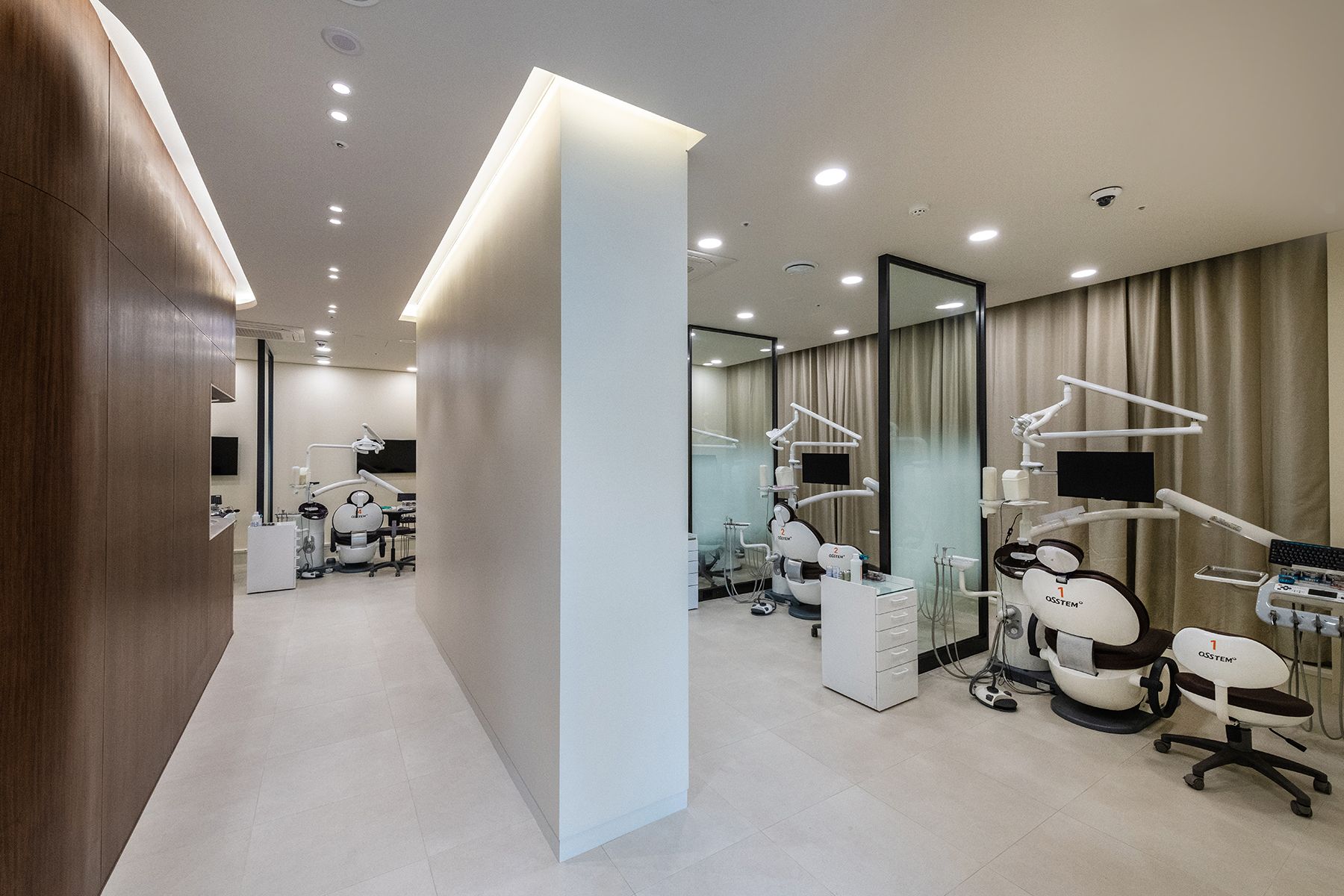 Modern dental clinic with white and wood accents; treatment rooms separated by glass and curtains.