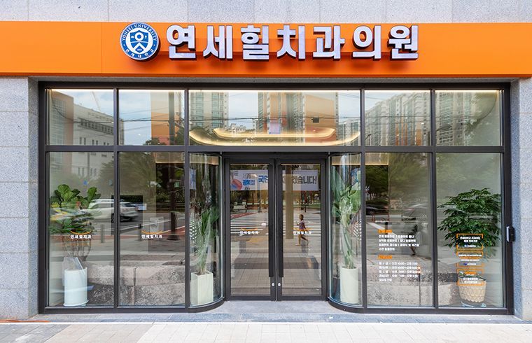 Dental clinic storefront with glass windows, an orange awning, and plants.