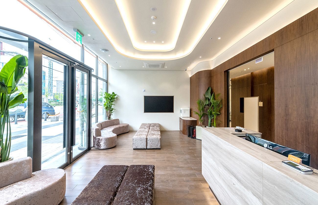 Modern waiting room with light wood and textured furniture, large windows, and a reception desk.