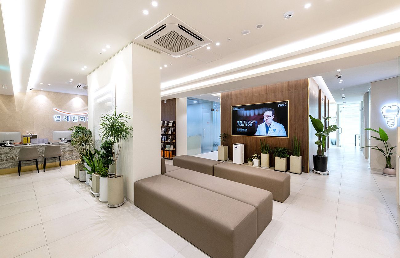 Modern clinic waiting area with benches, TV, plants, and reception desk.