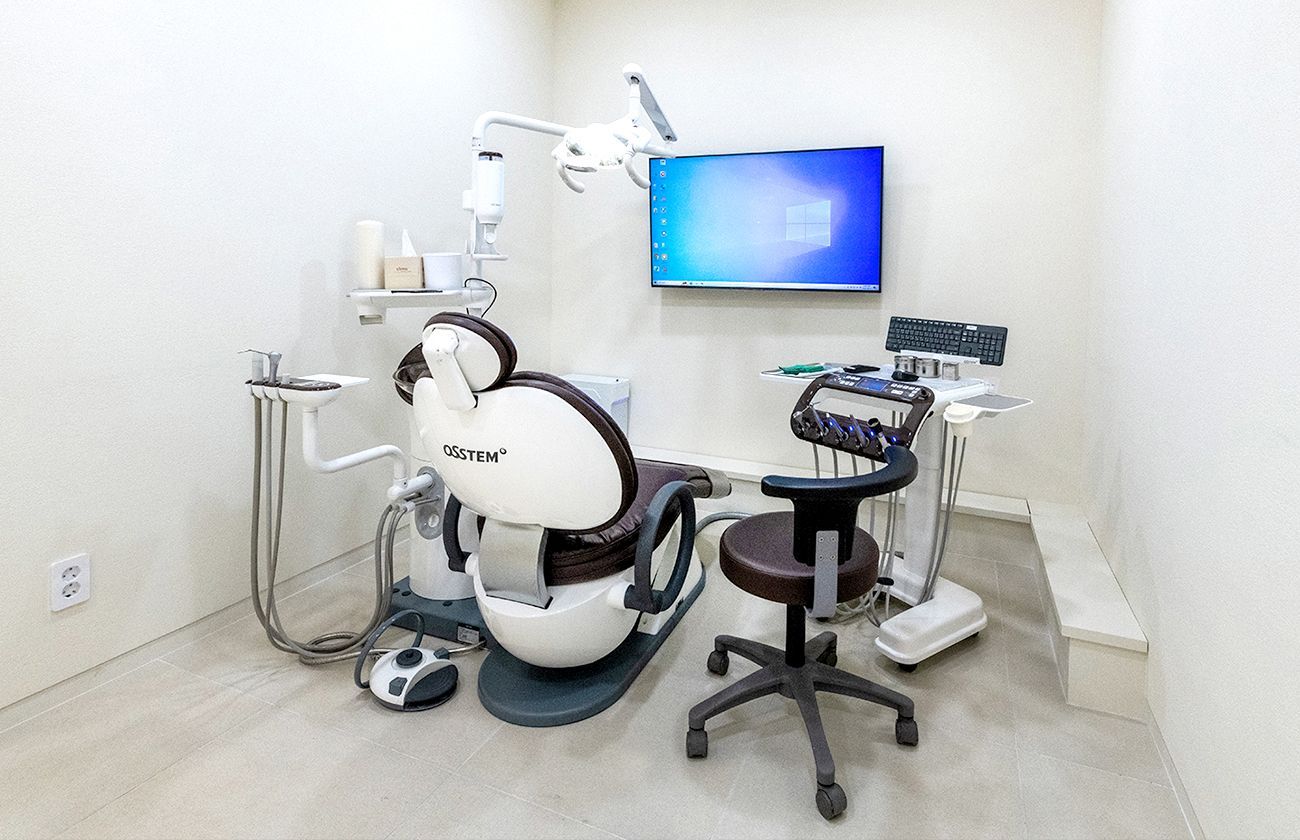 Dental office examination room with chair, equipment, and monitor on the wall.