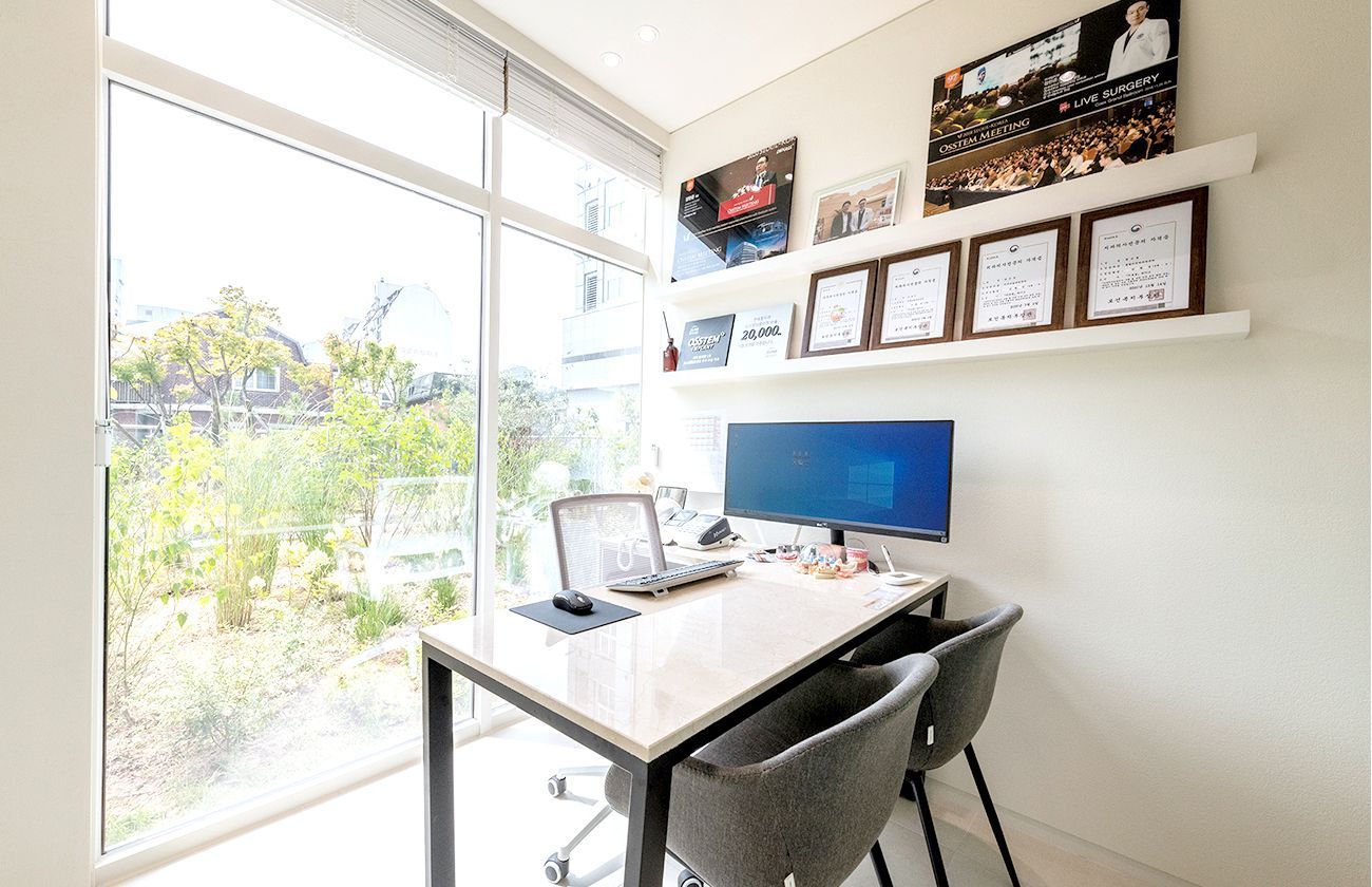 Home office with a desk, computer, chair, and window overlooking a garden. Framed pictures on wall.