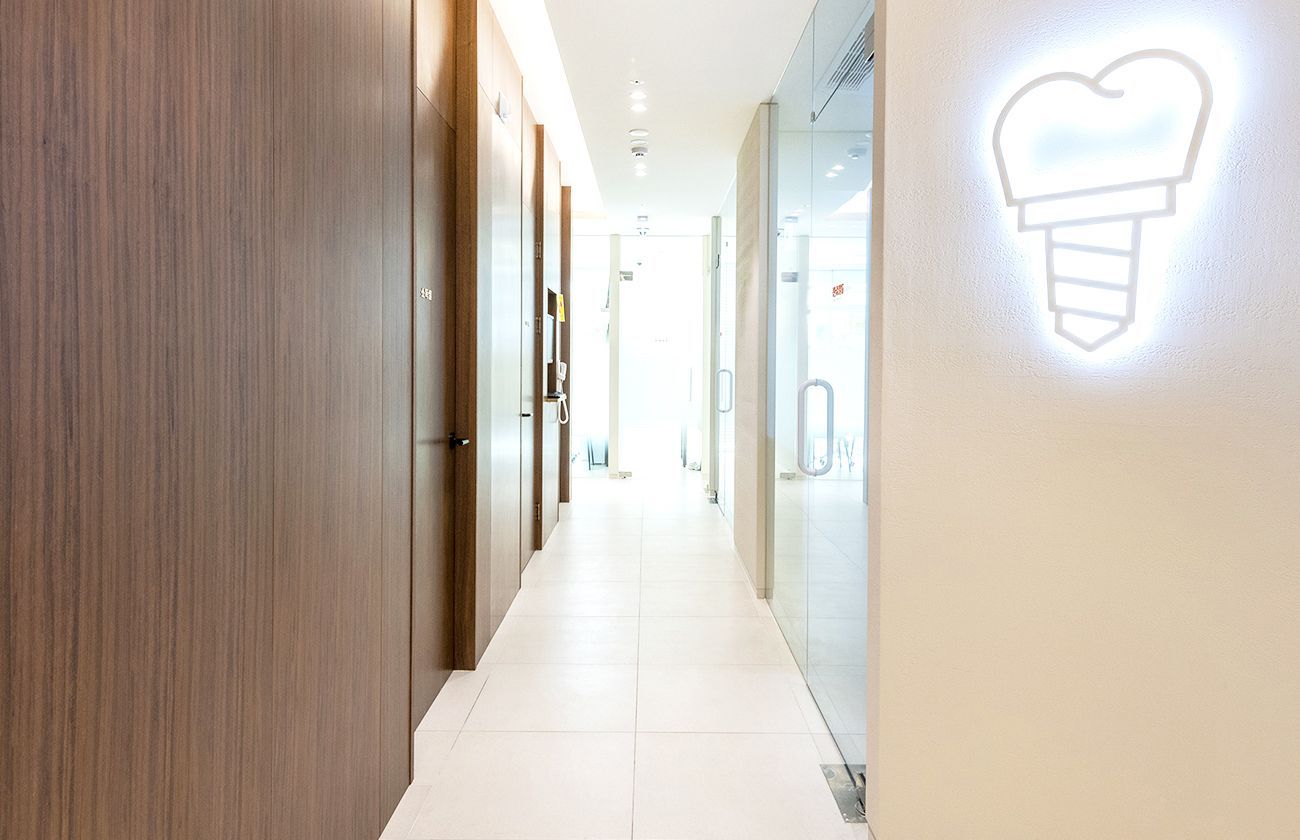 Hallway in a dental clinic with wood doors, a lit dental implant symbol, and bright light at the end.