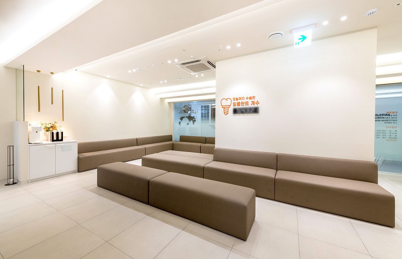 Spacious, well-lit waiting room with beige sofas, a white cabinet, and a reception sign.