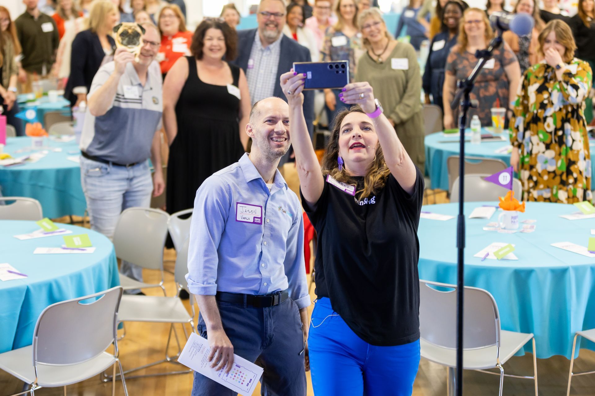 photo of two people taking a selfie with a crowd behind them