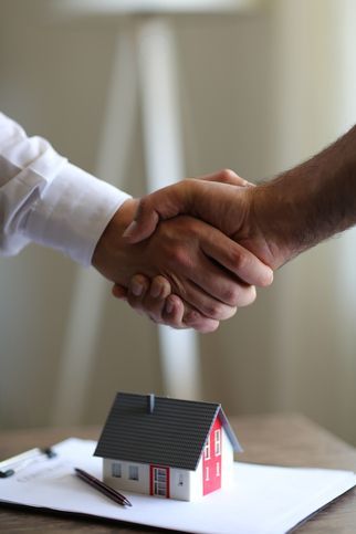 Handshake over a miniature house on documents, suggesting a real estate agreement