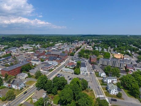 Aerial view of a small town with roads, buildings, trees, and a blue sky with clouds.