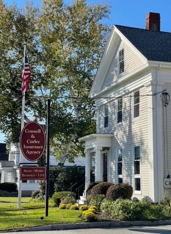 Red-brick inn with white columns and an American flag beside a sign under a blue sky.