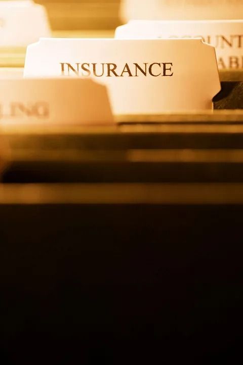Close-up of file folders, one labeled “INSURANCE,” in warm office lighting.