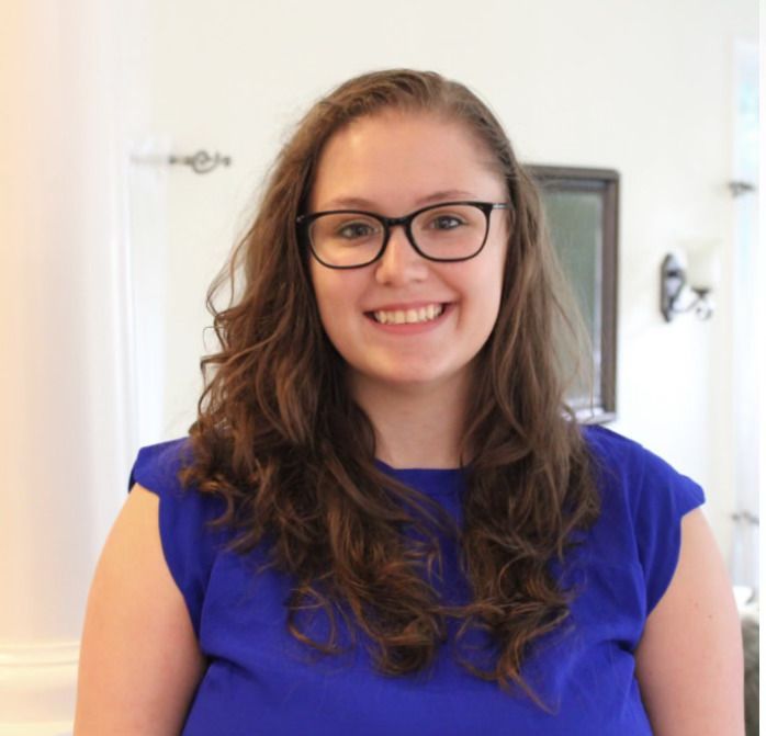 Woman in blue top and glasses smiles in well-lit room.